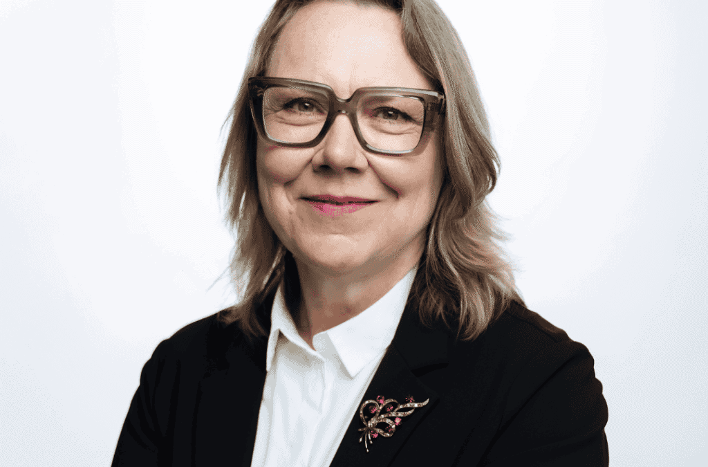 Professional woman in business attire with glasses smiling at camera.